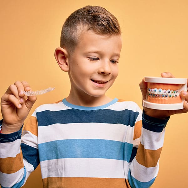 ChildOrthodontics Child holding braces and aligners